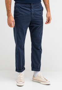 Marineblauwe katoenen broek met een elastische tailleband en opgerolde boorden. Gecombineerd met lichte sneakers met een contrasterende rode streep.