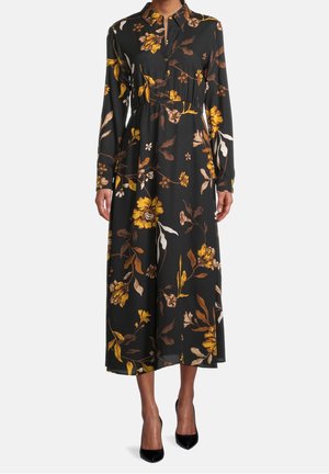 Czarna sukienka midi z długim rękawem, z żółto-brązowym kwiatowym wzorem, zapięta pod kołnierzyk na guziki, dopasowana w talii, noszona z czarnymi, czubkowatymi szpilkami.