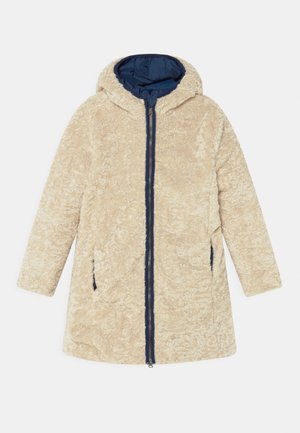 Beige textuurige capuchonjas met marineblauwe voering, ritssluiting aan de voorkant en twee zijzakken, plat gelegd op een witte achtergrond.