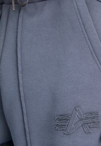 Ciemnoszare dresy o miękkiej fakturze, z subtelnie wyszytym logo na dolnej części nogawki oraz elastycznym paskiem ze sznurkiem.