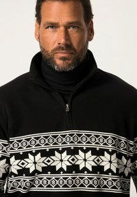 Suéter negro con cuello con cremallera, que presenta un patrón de copos de nieve blancos y geométrico en el pecho. Textura acanalada, tela cálida.