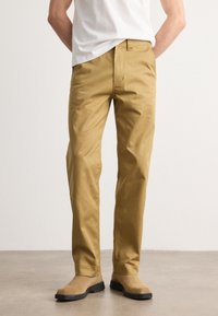 Beige chinos with a straight fit, made from smooth cotton fabric. Features belt loops, front pockets, and a clean design without visible branding.