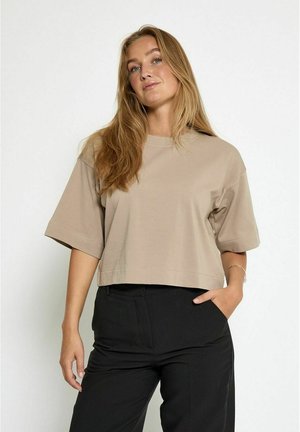 Cropped beige t-shirt made of soft fabric, featuring short sleeves, a round neckline, and a relaxed fit. Worn with black pants.