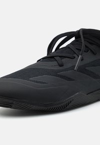 Black athletic shoe featuring synthetic upper, textured mesh panels, flat laces, and a contoured rubber sole with a tread pattern.