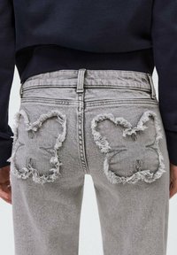 Harso denim farkut, joissa on revittyjä perhosmuotoja takataskuissa, klassisella viiden taskun muotoilulla ja vetoketjullisella taskulla.