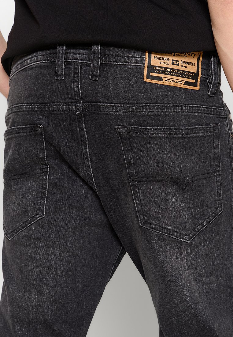 Dunkelgraue Denim-Jeans mit schmaler Passform. Sie verfügen über zwei Gesäßtaschen, kontrastierendes Nähen und ein braunes Etikett am Bund mit Text.