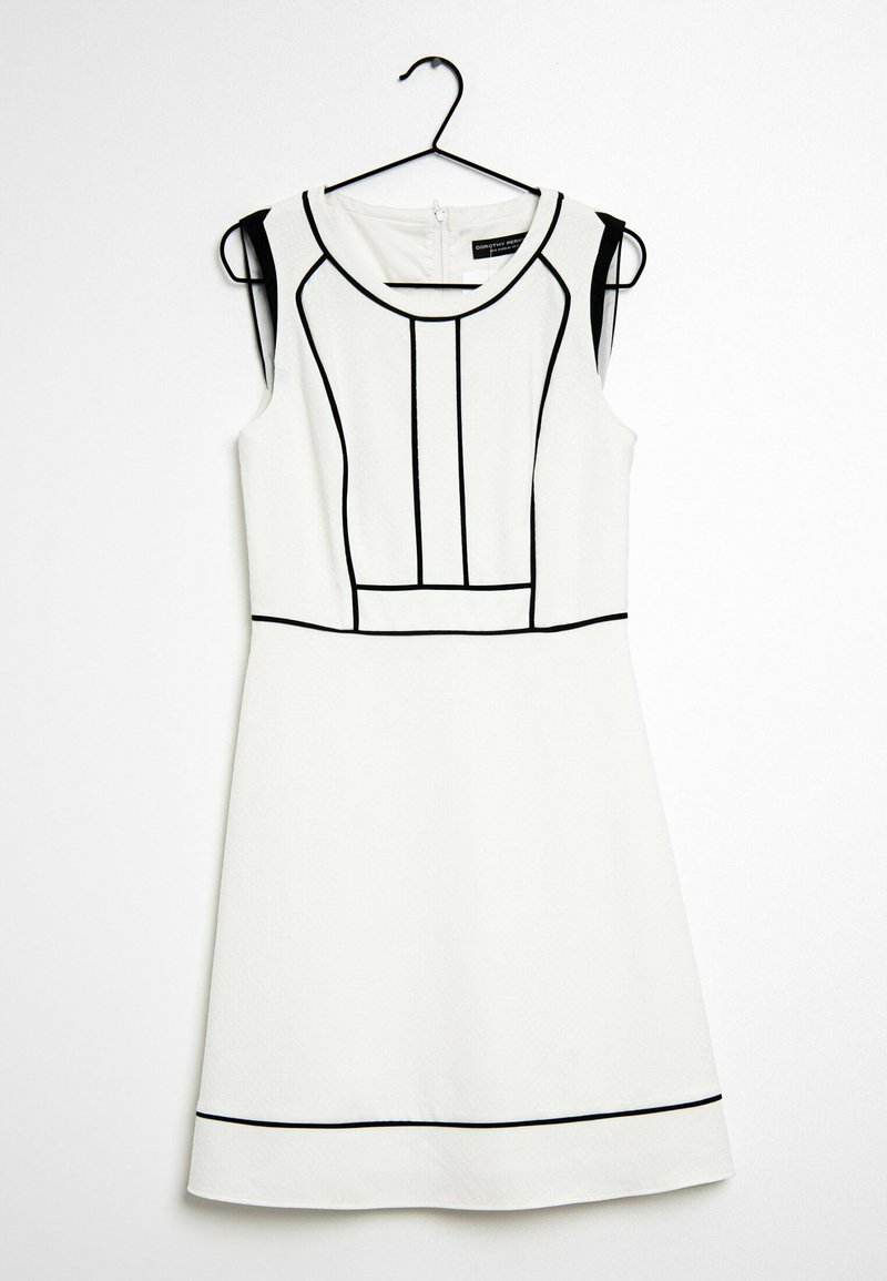Bezrukávové bílé šaty s černými geometrickými liniemi, kulatým výstřihem, strukturovanou tkaninou a zipovým zapínáním na zádech. Visí na černém háčku.