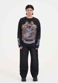 Zwarte sweatshirt met lange mouwen met een grafisch ontwerp van een paard en vlammen, gecombineerd met baggy zwarte broek en zwarte schoenen.