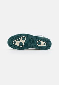Semelle d'une basket Puma en bleu sarcelle et beige avec des motifs de semelle circulaires et triangulaires sur fond blanc.