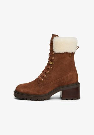 Bruine suede enkelboot met een bontkraag, gouden oogjes, dikke veters en een blokhak. Bevat een getextureerde buitenzool voor grip.