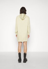 Huvtröja klänning i ljusgul med långa ärmar och ribbade muddar. Har en logotyp på baksidan och når precis ovanför knäet. Svarta plattform stövlar.