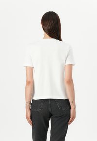 Witte T-shirt met korte mouwen, gemaakt van zacht katoen, met een ronde hals, een relaxte pasvorm en zichtbare stikdetails. Draagt met donkere spijkerbroek.