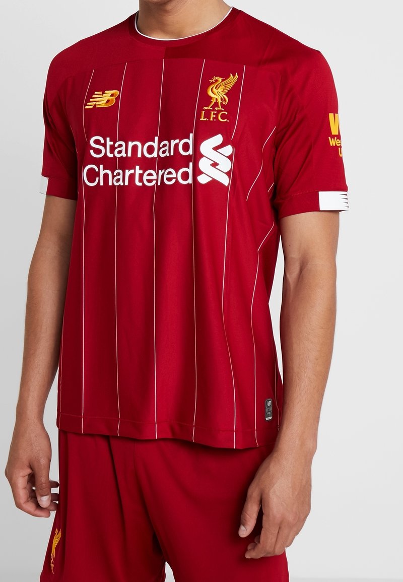 Röd Liverpool FC-tröja i lättviktsmaterial, med vita ränder, broderad logotyp och sponsortext på framsidan och ärmarna.