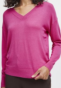 Pull rose à col en V en tissu tricoté doux. Comprend des manches longues, des poignets et un bas côtelés, avec une coupe décontractée et une texture lisse.