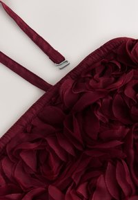 Bordeaux rode tas met een bloemenpatroon gemaakt van laagjes stoffen blaadjes, met een zilverkleurige metalen gesp en verstelbare bandjes. Gestructureerd oppervlak.