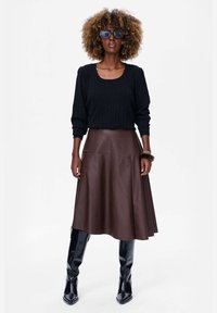 Brązowa skórzana spódnica w kształcie litery A połączona z czarną, prążkowaną bluzką z długim rękawem oraz czarnymi, wysokimi na kolana kozakami. Dodatki to okulary przeciwsłoneczne i bransoletka.