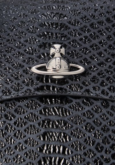 Ασημένιο σφαιρικό αντικείμενο με σταυρό και έμβλημα δαχτυλιδιού πάνω σε υφή με μαύρο μοτίβο που μοιάζει με δέρμα ερπετού, πιθανώς λεπτομέρεια σχεδιαστικού αξεσουάρ.