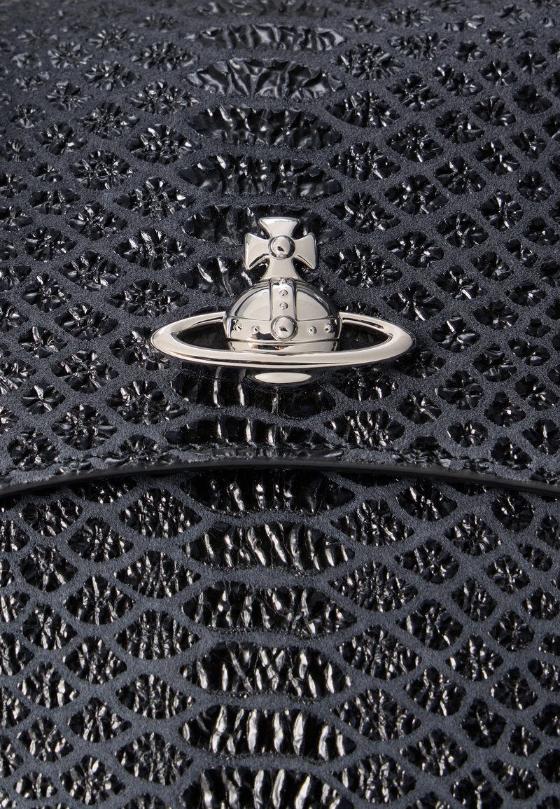 Sfera d'argento con emblema a croce e anello su superficie nera strutturata a motivi, simile alla pelle di un rettile, probabilmente dettaglio di un accessorio di design.