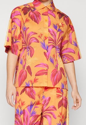 Koszula z krótkim rękawem na guziki oraz dopasowane spodnie z wyrazistym wzorem tropikalnych liści w kolorach różowym, czerwonym i fioletowym na pomarańczowym tle.