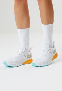 Valkeat urheilukengät, joissa on teksturoitu kangas päällinen, oranssit yksityiskohdat pohjassa ja mintunvihreät yksityiskohdat varpaassa. Yhdistetty valkoisten, uurrettujen sukkien kanssa.