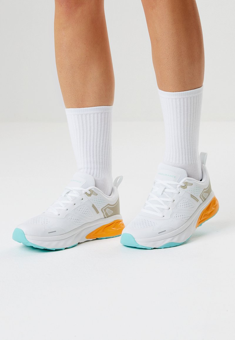 Valkeat urheilukengät, joissa on teksturoitu kangas päällinen, oranssit yksityiskohdat pohjassa ja mintunvihreät yksityiskohdat varpaassa. Yhdistetty valkoisten, uurrettujen sukkien kanssa.