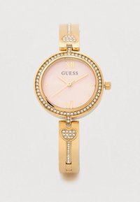 Guldur med rund urskive, lyserød skive og gyldne accenter. Har krystalpynt og et hjerteformet led i armbåndets design.