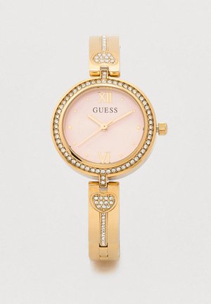 Gouden horloge met een ronde wijzerplaat, roze wijzerplaat en gouden accenten. Heeft kristallen versieringen en een hartvormige schakel in het armbandontwerp.