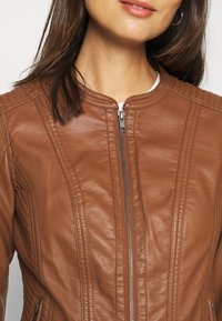 Giubbotto in pelle marrone con collo rotondo, zip frontale e pannelli laterali trapuntati. Texture liscia con dettagli di cucitura visibili.