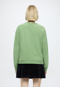 Sweatshirt verde com decote redondo e mangas raglan, combinado com uma saia de veludo cotelê preta com detalhes plissados.