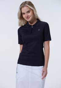 Navy-Polohemd mit kurzen Ärmeln, aus leichtem Material, mit Reißverschlusskragen und Logodetail auf der linken Brust; kombiniert mit einem weißen Rock.