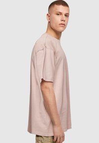 Overdimensioneret lyserød T-shirt lavet af blødt stof, med rund halsudskæring og korte ærmer, præsenteret i en sideprofil.