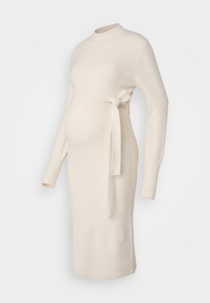 Vestido de maternidade em malha canelada de cor creme, com mangas longas, decote redondo e detalhe de cintura amarrada. Textura suave, design ajustado ao corpo.