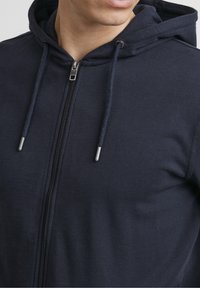 Sweat à capuche zippé bleu marine en tissu doux, doté d'une capuche avec cordon de serrage, d'une fermeture éclair en métal et de poignets côtelés pour un ajustement confortable.