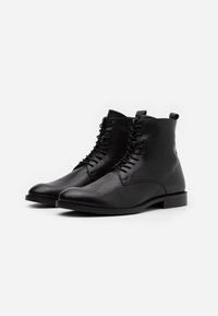 Botines de cuero negro con punta redondeada, cordones en el frente y tacón bajo cuadrado. Textura suave con detalles de costura mínimos.