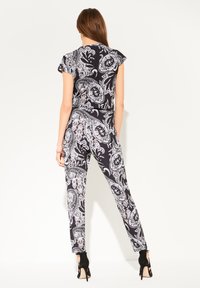 Conjunto con patrón de paisley en blanco y negro, blusa de manga corta y pantalones ajustados, tejido suave, diseño elegante, complementado con zapatos de tacón alto negros.