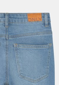 Jeans in denim azzurro chiaro con un'etichetta in pelle marrone con la scritta "ONLY." Presentano due tasche posteriori con cuciture a contrasto e un taglio dritto classico.