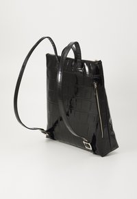 Bolso de mano de charol negro con un patrón de cocodrilo texturizado, que cuenta con dos asas y un bolsillo con cremallera en el costado.
