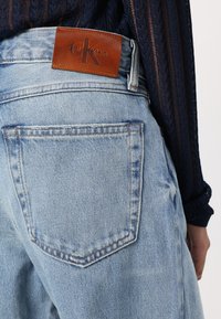 Jeans de mezclilla azul claro con una cintura alta, corte recto y una etiqueta de cuero marrón de Calvin Klein en la parte trasera de la cinturilla.