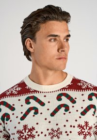 Gebreid Kersttrui met een crèmekleurige basis en rode en groene kerststok en sneeuwvlokpatronen. Klassiek ontwerp met ronde hals en ribgebreide randen.