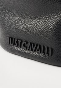 Juodas tekstūruotas odinis rankinės modelis, kuriame iškilęs blizgus "JUST CAVALLI" logotipas priekyje. Medžiaga turi akmenėlių pavidalo raštą.