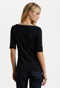 Zwarte, korte mouwen top met een brede halslijn en omgeslagen mouwen. Gladde textuur, getailleerd ontwerp, gecombineerd met donkerblauwe jeans. Eenvoudig en veelzijdig.