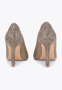Błyszczące szpilki z zaostrzonym noskiem, z metalicznie złotą i srebrną tkaniną w plecionkę, smukłymi obcasami w kształcie szpilki oraz gładką beżową podeszwą.