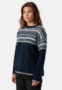 Sininen neulepaita, jossa on Fair Isle -kuvio valkoisena, harmaana ja kermaisenä rinnan kohdalla, sekä ribbaa hihansuissa ja helmasssa.