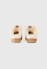 Cream-colored fluffy slip-on shoes with a tan rubber sole and decorative woven accent on the back. Soft texture and open back design.