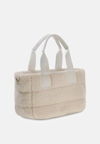 Kremowa torba na ramię z fakturowanego, pluszowego materiału, z białymi tkaninowymi uchwytami i metalowym akcentem z boku.