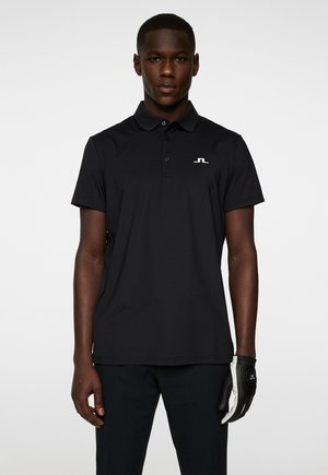 Polo shirt nera con maniche corte e colletto. Presenta un piccolo logo bianco sul lato sinistro del petto. Tessuto dalla texture liscia.