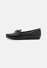 Chaussure plate noire avec un design en cuir texturé, bout rond et un accent en nœud sur l'empeigne, avec une semelle discrète.