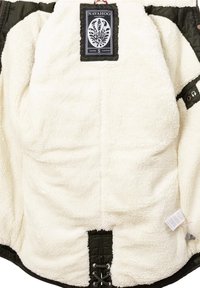 Veste verte doublée en polaire avec un intérieur crème, dotée d'une taille à cordon de serrage et d'une étiquette de marque. Coutures piquées et tissu texturé.