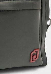 Grau Rucksack aus strapazierfähigem Stoff, mit strukturiertem Oberflächen und einem auffälligen roten Logoakzent auf der Vorderseite.
