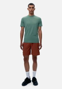 Gaiši zaļa sporta t-krekls ar īsām piedurknēm, apvienots ar rūsas krāsas šortiem. Melni sporta apavi un baltas zeķes ar rakstu noslēdz kopskatu.